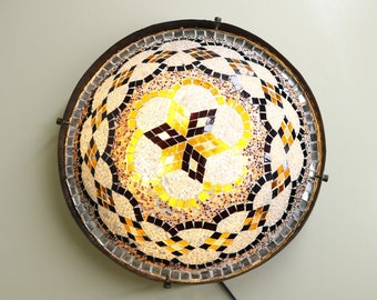 May include: A round, mosaic-style ceiling light fixture with a geometric pattern in shades of brown, black, and gold. The light is illuminated, casting a warm glow.