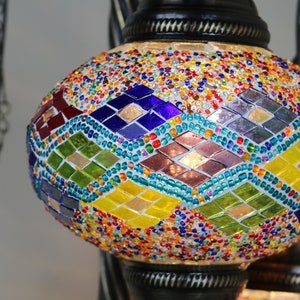 May include: A colorful mosaic glass pendant light with a diamond pattern. The light is made of small, colorful glass pieces and is hanging from a chain.
