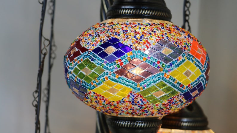 May include: A colorful mosaic glass pendant light with a diamond pattern. The light is made of small, colorful glass pieces and is hanging from a chain.