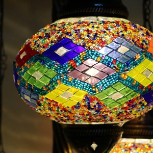 May include: A colorful mosaic glass lampshade with a geometric pattern in shades of blue, green, yellow, and purple. The lampshade is round and has a metallic base.