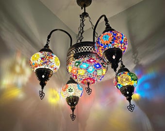 May include: A multi-colored mosaic glass chandelier with five globe-shaped lamps. The lamps are suspended from a dark metal frame and chain. The mosaic glass features a variety of colors, including red, blue, yellow, and green. The chandelier is hanging from the ceiling.