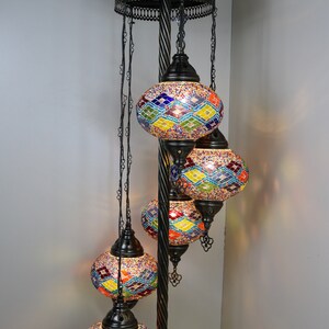 May include: A black metal floor lamp with a decorative top and five hanging mosaic glass globes. The globes are multicolored with a diamond pattern and are lit from within.