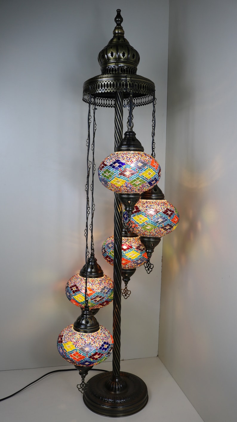 May include: A black metal floor lamp with a decorative top and five hanging mosaic glass globes. The globes are multicolored with a diamond pattern and are lit from within.