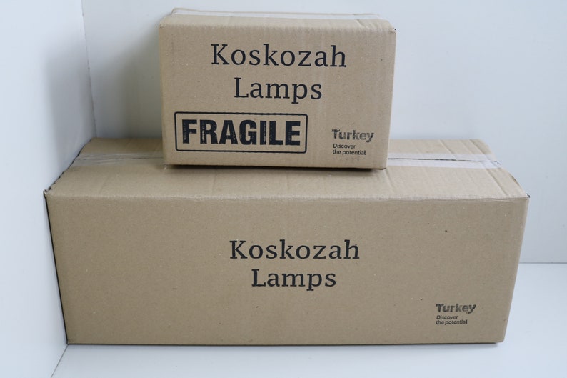 May include: Two brown cardboard boxes stacked on top of each other. The top box has the text "Koskozah Lamps" and "FRAGILE" printed on it. The bottom box has the text "Koskozah Lamps" printed on it. Both boxes have a sticker that says "Turkey Discover the potential."