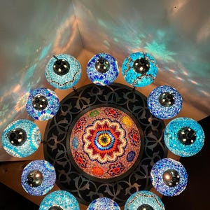 May include: A ceiling light fixture with a central dome surrounded by 12 smaller globes. The dome is made of colorful mosaic tiles and the globes are made of blue mosaic tiles.