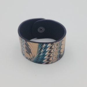 May include: A black leather cuff bracelet with a marbled design in shades of beige, teal, black, and white.