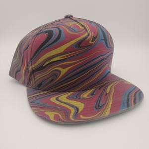 May include: A red, blue, yellow, and black marbled patterned baseball cap. The cap has a flat brim and a structured crown.