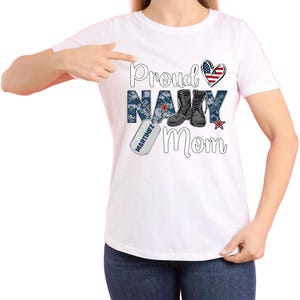May include: White t-shirt with the text "Proud Navy Mom" in blue and black lettering. The text is surrounded by a camouflage pattern and a red, white, and blue heart. A dog tag with the text "MARTINEZ" is hanging from the bottom of the "Navy" text.