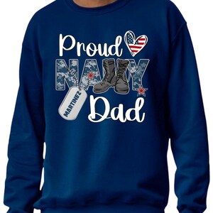 May include: Navy blue sweatshirt with a white graphic that says "Proud Navy Dad" with a red, white, and blue heart, a pair of boots, and a dog tag that says "Martinez".