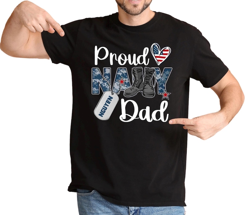 May include: Black t-shirt with a white graphic that says "Proud Navy Dad" with a red heart, an American flag, and a military boot design. The graphic also includes a dog tag with the name "NGUYEN" on it.