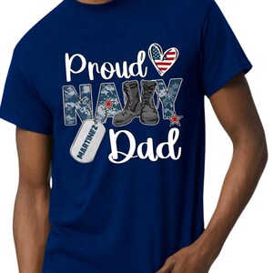 May include: Navy blue t-shirt with a white heart with an American flag design, the words "Proud Navy Dad" and a boot with a dog tag that says "Martinez".