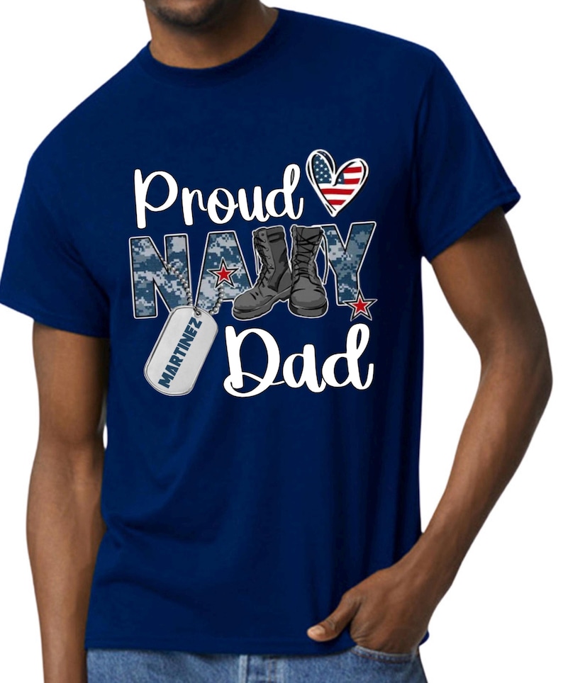 May include: Navy blue t-shirt with a white heart with an American flag design, the words "Proud Navy Dad" and a boot with a dog tag that says "Martinez".
