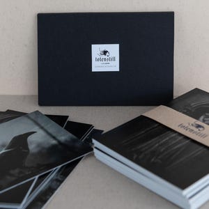 May include: A stack of black and white photo cards with a black envelope. The envelope has a white label with the text "tolen still" and "compilation 19".