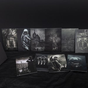 May include: A set of eight black and white photographic prints featuring various gothic and cemetery scenes. The prints are arranged in two rows of four, with a black box in the foreground. The prints depict a variety of subjects, including a church, a graveyard, a statue of an angel, and a gate.