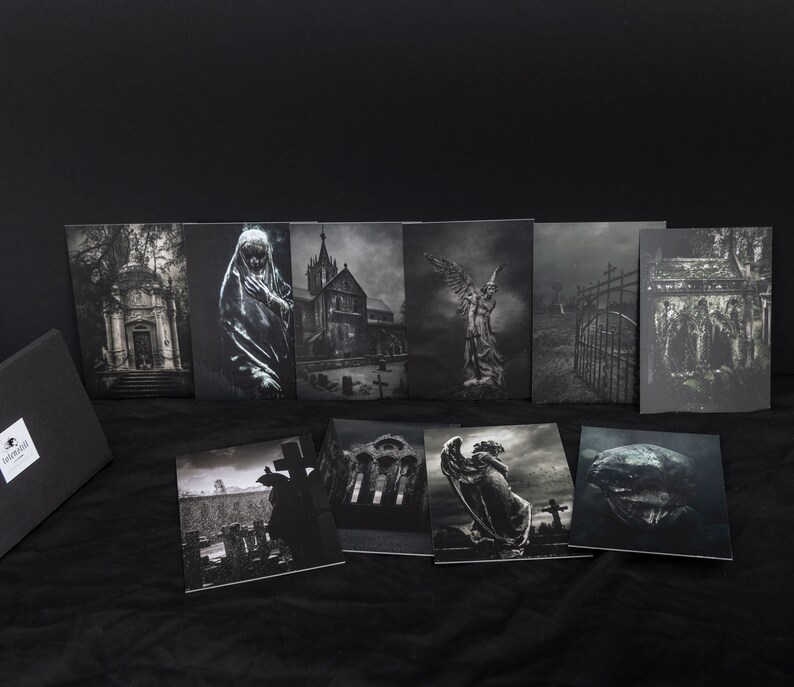 May include: A set of eight black and white photographic prints featuring various gothic and cemetery scenes. The prints are arranged in two rows of four, with a black box in the foreground. The prints depict a variety of subjects, including a church, a graveyard, a statue of an angel, and a gate.