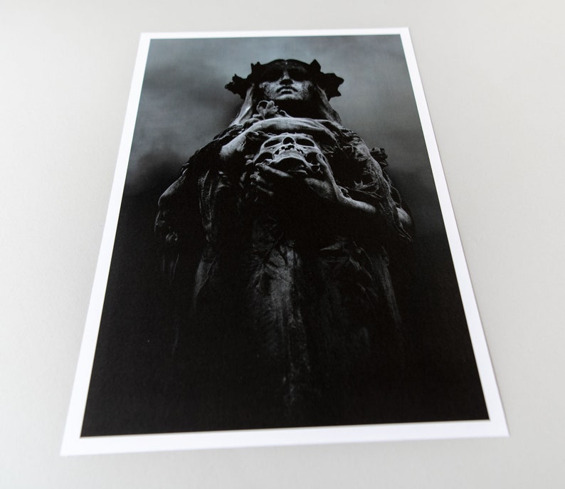 May include: A black and white photograph of a statue of a woman wearing a crown and holding a skull. The statue is in a dark, shadowy setting.