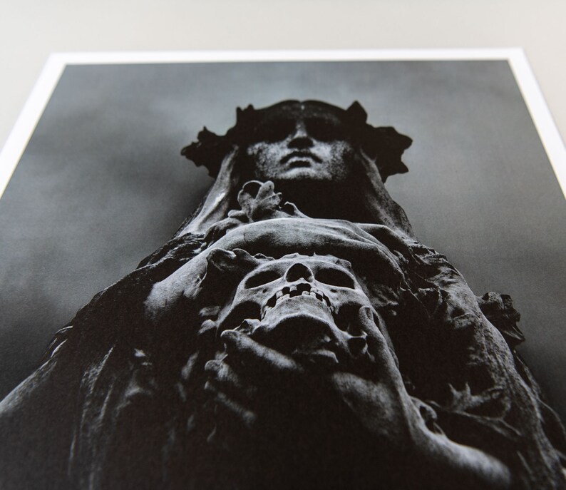 May include: A black and white photograph of a stone sculpture of a woman wearing a crown of thorns and holding a skull in her hands.