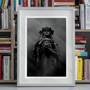 May include: A black and white photograph of a statue of a woman with a crown of thorns holding a skull in her hands. The statue is in a dark, shadowy setting.