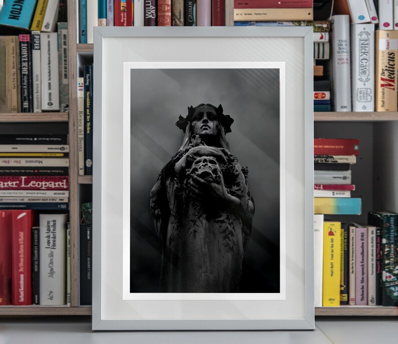 May include: A black and white photograph of a statue of a woman with a crown of thorns holding a skull in her hands. The statue is in a dark, shadowy setting.