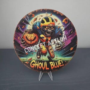 May include: Circular wooden sign depicting a zombie American football player holding a pumpkin. The sign features the text "CONCEPT ASYLUM" and "GHOUL BLUE!" in a colourful, spooky design. The background includes autumn leaves and a stadium.