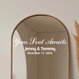 May include: A gold-framed arched mirror with the text "Your Seat Awaits" in white cursive lettering. Below the text, it reads "Jenny & Tommy" and "December 17, 2025".