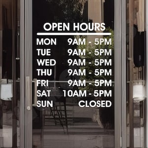 May include: A white sign with black text on a glass door, displaying the business hours. The sign reads "OPEN HOURS" and lists the hours of operation for each day of the week. Monday through Friday, the business is open from 9 AM to 5 PM. On Saturday, the business is open from 10 AM to 5 PM. On Sunday, the business is closed.