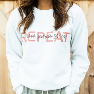 May include: White sweatshirt with the text "REPEAT" in large red letters and the words "coffee create sleep" in smaller black letters underneath.