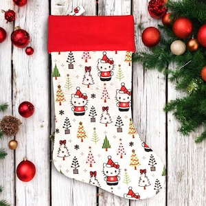 May include: A Christmas stocking with a red cuff and a pattern featuring Hello Kitty characters in Santa hats and Christmas trees on a white background. The stocking is decorated with red and green accents.