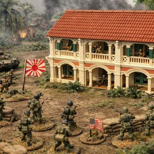 Op de afbeelding: Gedetailleerd diorama met een militaire scène met miniatuursoldaten, een gebouw met twee verdiepingen met een rood pannendak en een Japanse vlag. Een tank is zichtbaar op de achtergrond en zandzakken op de voorgrond.
