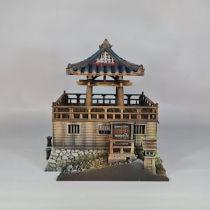 K&ouml;nnte beinhalten: Ein detailliertes Miniaturmodell einer japanischen Pagode mit einem mehrstufigen Dach und einer aufwendigen Holzkonstruktion. Das Modell hat ein blaues und goldenes Dach und einen Steinsockel. Die Pagode steht vor einem schlichten Hintergrund.
