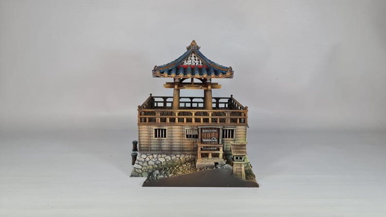 K&ouml;nnte beinhalten: Ein detailliertes Miniaturmodell einer japanischen Pagode mit einem mehrstufigen Dach und einer aufwendigen Holzkonstruktion. Das Modell hat ein blaues und goldenes Dach und einen Steinsockel. Die Pagode steht vor einem schlichten Hintergrund.