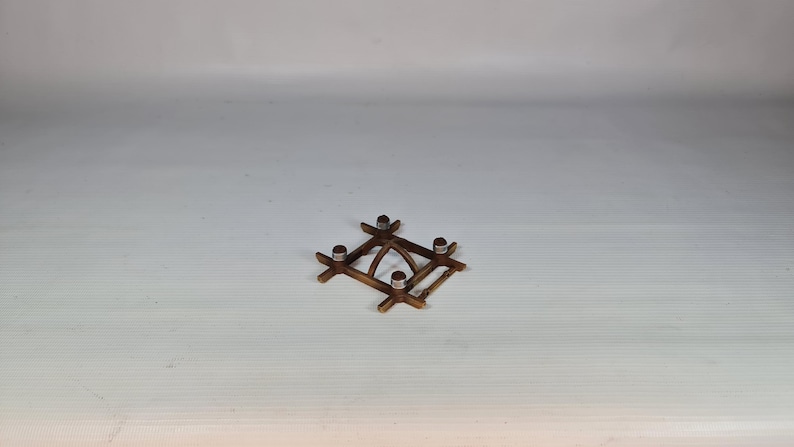 K&ouml;nnte beinhalten: Ein kleiner, quadratischer Kerzenhalter aus Holz mit vier Metallkerzenschalen. Der Halter ist aus dunkelbraunem Holz gefertigt und hat ein einfaches, geometrisches Design. Der Kerzenhalter ist ca. 10 cm breit und 10 cm lang.