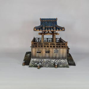 K&ouml;nnte beinhalten: Miniatur-Pagode im japanischen Stil mit blauem Ziegeldach und Holzstruktur. Die Pagode hat mehrere Ebenen, darunter einen Balkon und einen Steinsockel. Das Modell ist detailliert mit aufwendigen architektonischen Elementen gestaltet, vor wei&szlig;em Hintergrund.