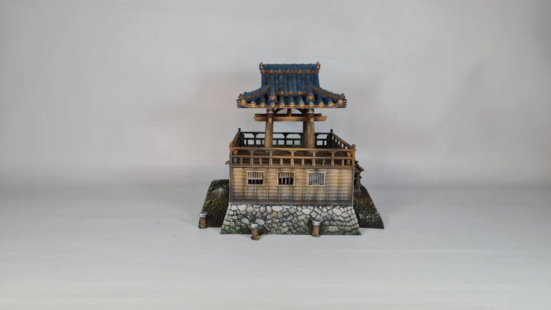 K&ouml;nnte beinhalten: Miniatur-Pagode im japanischen Stil mit blauem Ziegeldach und Holzstruktur. Die Pagode hat mehrere Ebenen, darunter einen Balkon und einen Steinsockel. Das Modell ist detailliert mit aufwendigen architektonischen Elementen gestaltet, vor wei&szlig;em Hintergrund.