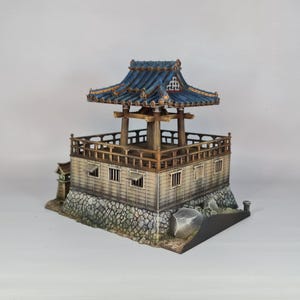K&ouml;nnte beinhalten: Miniatur-Pagode im japanischen Stil mit blauem Ziegeldach und Holzst&uuml;tzen. Die Struktur hat ein mehrst&ouml;ckiges Design mit detailliertem Gel&auml;nder und Steinsockel. Die Pagode ist ein Modell eines traditionellen japanischen Geb&auml;udes.