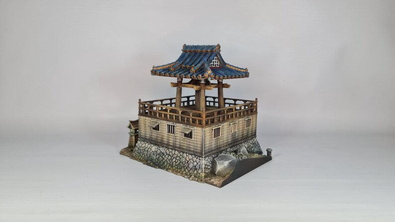 K&ouml;nnte beinhalten: Miniatur-Pagode im japanischen Stil mit blauem Ziegeldach und Holzst&uuml;tzen. Die Struktur hat ein mehrst&ouml;ckiges Design mit detailliertem Gel&auml;nder und Steinsockel. Die Pagode ist ein Modell eines traditionellen japanischen Geb&auml;udes.