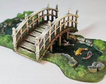 May include: A miniature wooden bridge with a brown and white paint finish spans a small pond with green grass and rocks. The pond is decorated with three orange and white koi fish.