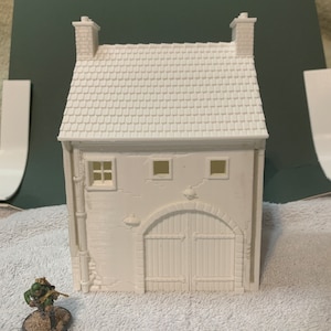 May include: A white, unpainted, 3D printed model of a small building with a tiled roof, two chimneys, and a large arched doorway. The building has two windows on the front and a small, rectangular window on the side.