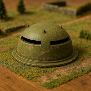 May include: A weathered, olive-green miniature bunker with two horizontal slits for viewing. The dome-shaped structure has three small, metal protrusions on top and sits on a circular base. The model is placed on a grassy surface.
