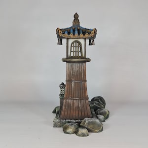 May include: A detailed miniature pagoda with a brown wooden tower, a blue and gold roof, and a small window. The pagoda is set on a base of rocks and is a decorative item.