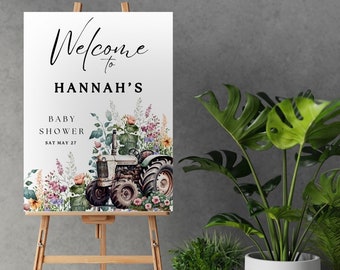 May include: Welcome to Hannah's Baby Shower sign with a watercolor illustration of a tractor in a field of flowers. The sign is on a wooden easel.