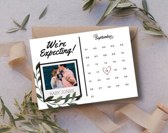 May include: A white card with a black border and green leaves around the edges. The card says "We're Expecting!" and has a photo of a couple holding an ultrasound image. The card also has a calendar with a heart around the 18th of September.
