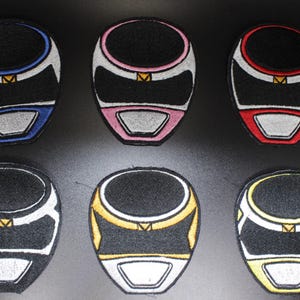 Puede incluir: Seis parches bordados con forma de cascos de Power Rangers. Cada casco tiene un fondo negro con detalles blancos, azules, rosas, rojos, amarillos y dorados. Los parches son probablemente para ropa o accesorios.
