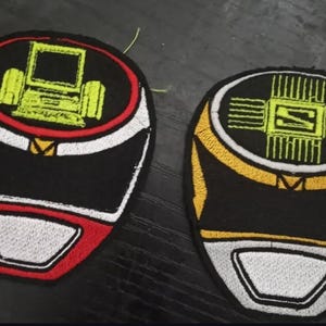 Pode incluir: Dois patches bordados com designs de capacete. Um é preto com detalhes vermelhos e brancos e um gráfico de computador amarelo. O outro é preto com detalhes amarelos e brancos e um gráfico amarelo.