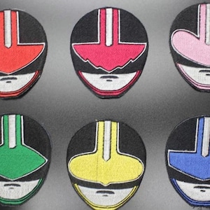 Könnte beinhalten: Sechs gestickte Aufnäher mit Power Ranger Helm-Designs. Jeder Aufnäher hat einen schwarzen Hintergrund mit einem farbigen Helmdesign in Rot, Rosa, Grün, Gelb und Blau. Die Helme haben weiße und silberne Akzente.