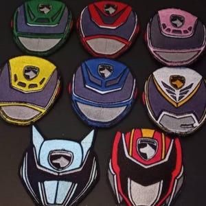 Puede incluir: Una colección de nueve parches bordados coloridos con diseños de cascos estilizados. Los parches muestran una variedad de colores, incluyendo verde, rojo, rosa, amarillo, azul y blanco, con costuras detalladas y un emblema central.