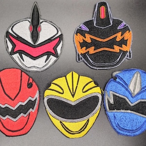 May include: Five embroidered patches depicting superhero helmet designs in various colours. The patches feature red, yellow, blue, black, and white. Each patch has a unique design with detailed stitching.