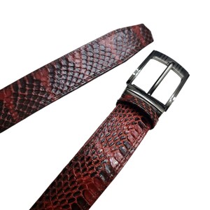 Może przedstawiać: Czerwono-czarny pasek ze wzorem sk&oacute;ry węża ze srebrną klamrą. Pasek wykonany jest z teksturowanego materiału i jest prezentowany na białym tle. Klamra ma prostokątny kształt z pojedynczym bolcem.