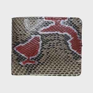 May include: A bi-fold wallet with a snakeskin pattern in shades of brown, black, and white. A red and white design is painted on the front of the wallet. The wallet is rectangular and appears to be made of leather.