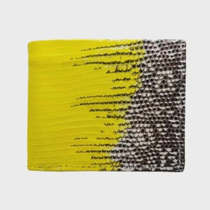 以下が含まれることがあります： 爬虫類のような質感の模様が施された二つ折り財布。左側は鮮やかな黄色で、右側は白と黒の模様に変わります。財布は長方形で、革製のように見えます。